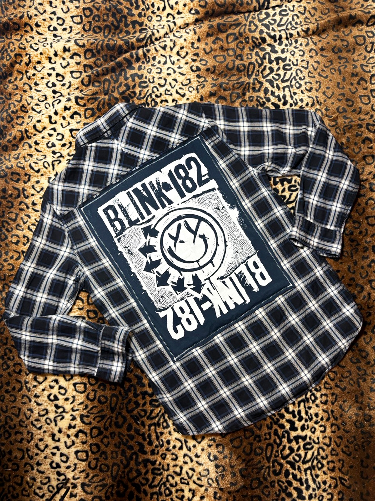 Plaid shirt with Blink-182 logo on a leopard print background