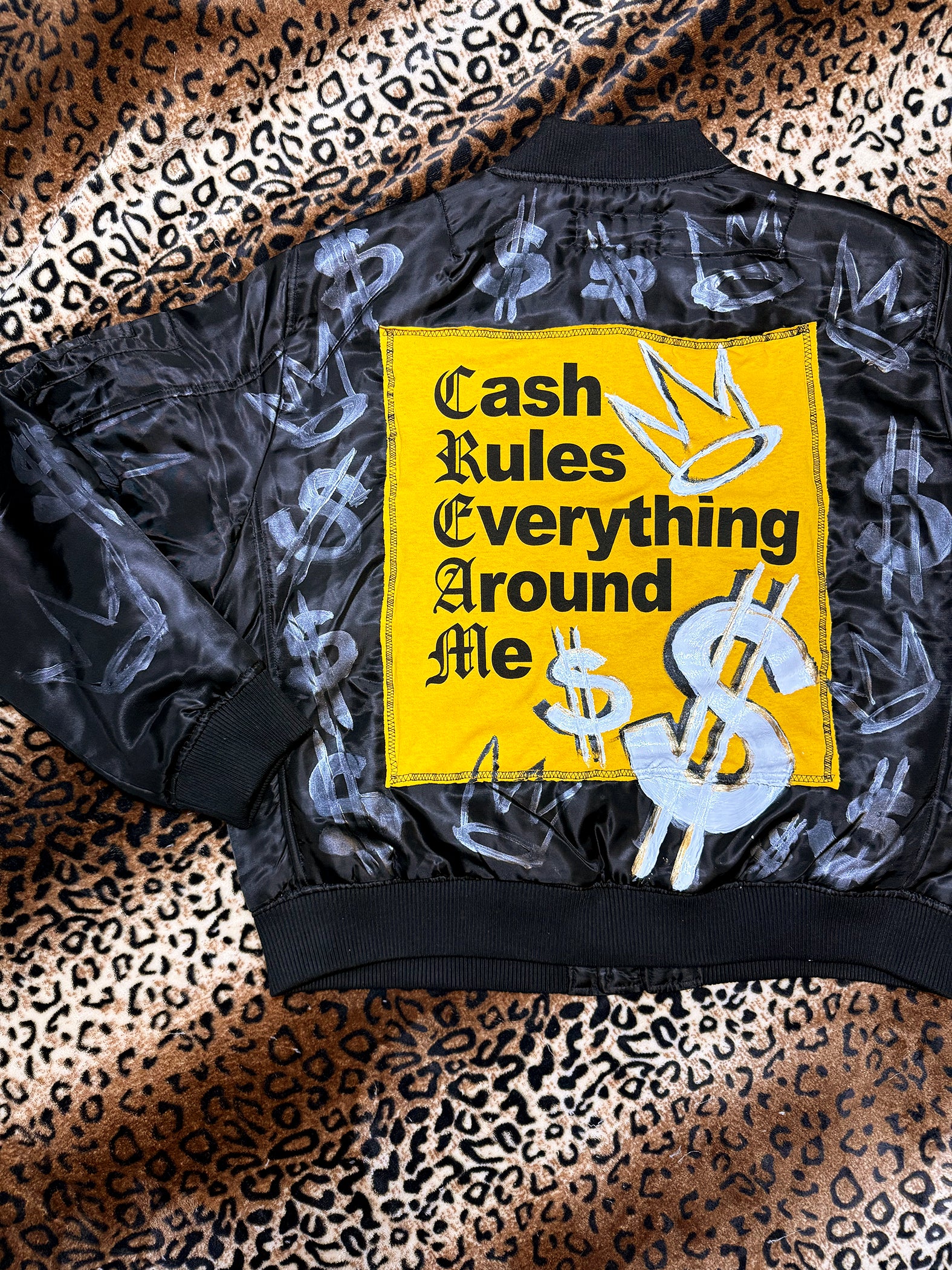 Black jacket with a yellow patch featuring text and dollar signs on a leopard print background