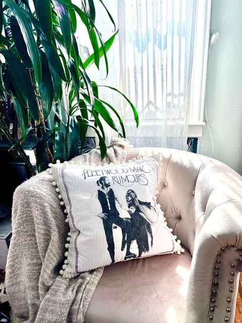 fleetwood mac throw pillow on blush colored chair with plant in the background top view